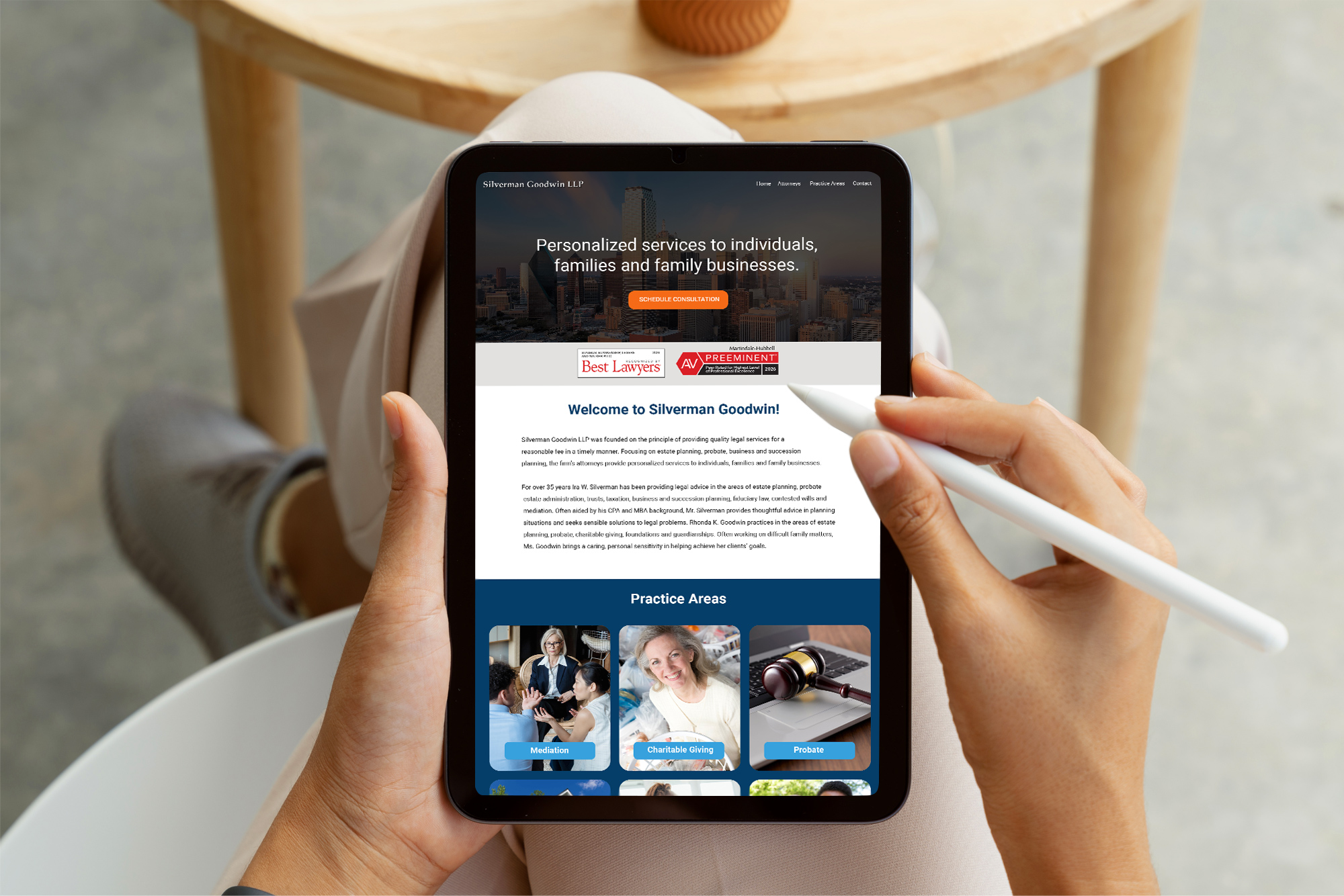 Hands holding tablet displaying redesigned homepage mockups with practice areas and trust badges for Silverman Goodwin LLP.