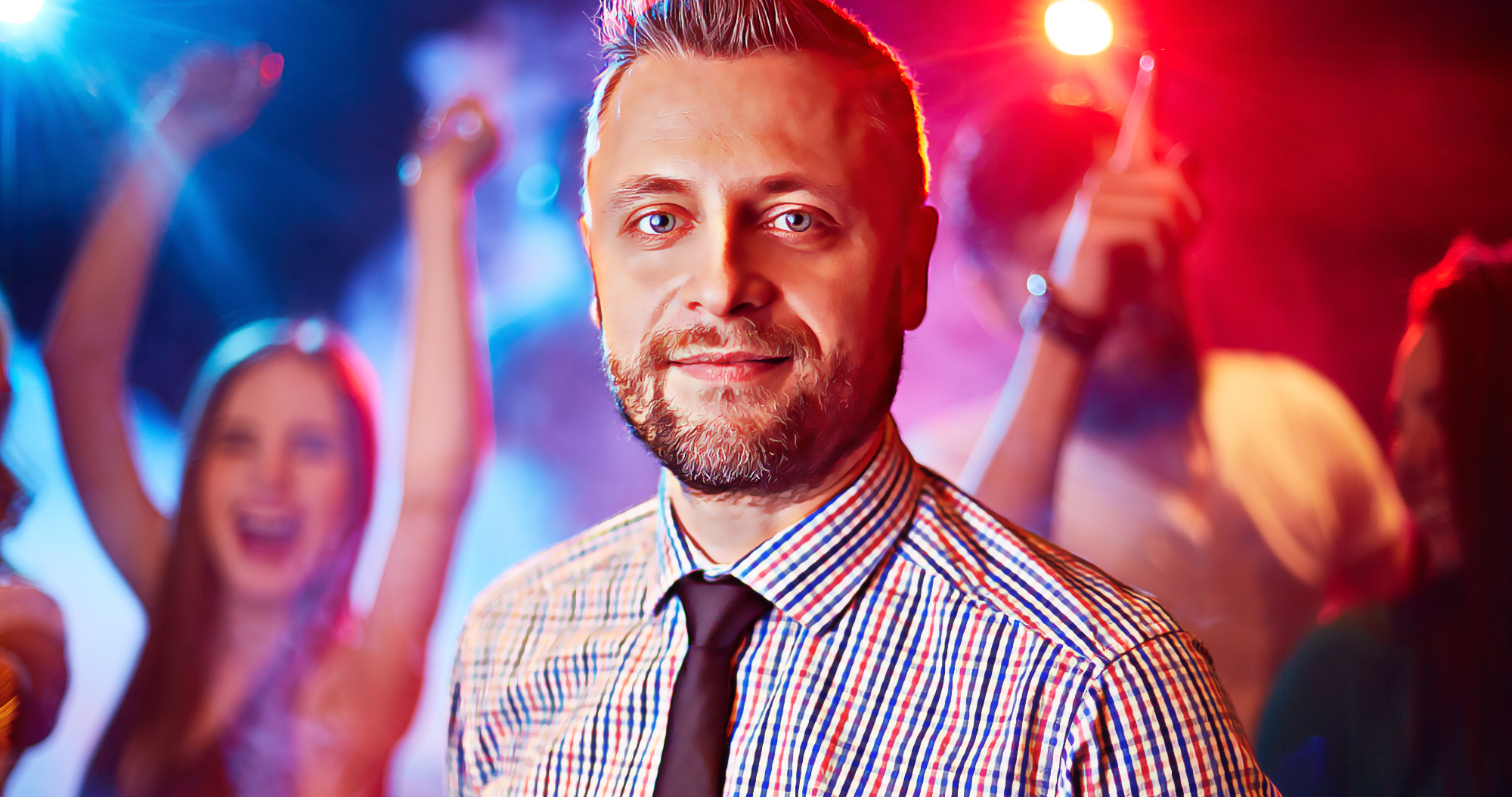 Man smiling at a colorful corporate party celebration with colleagues dancing in the background for employer branding event videography.
